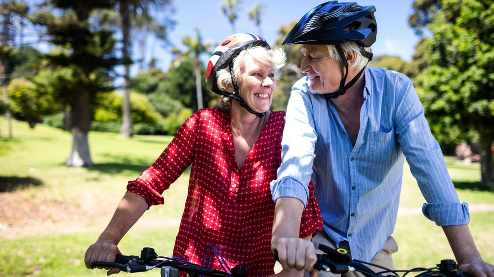 casal de idosos sorri ao andar de bicicleta. exercícios físicos reduzem risco de depresão