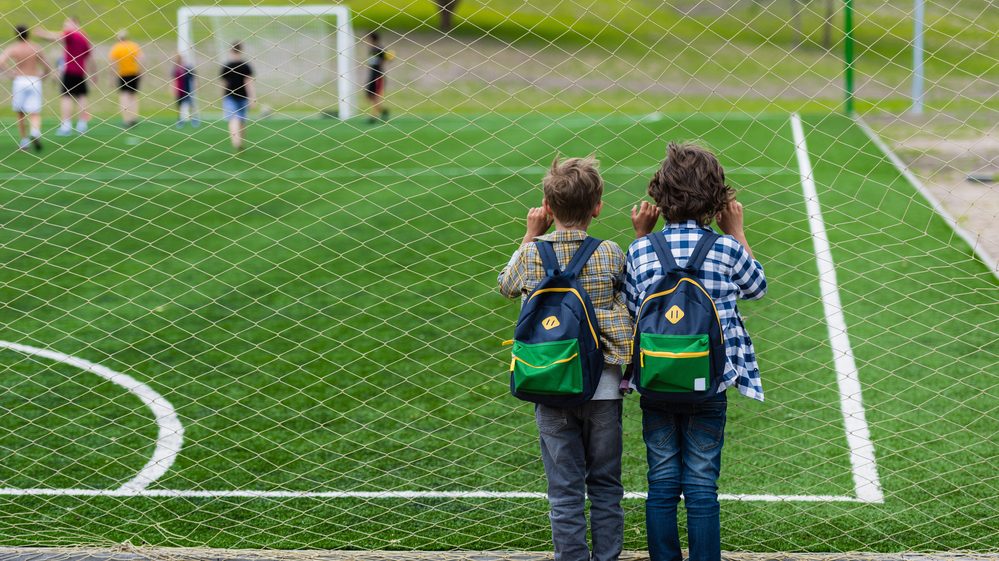 dois meninos de costas, assistem à partida de futebol próximos á rede. cosme e damião eram amigos desde a infância