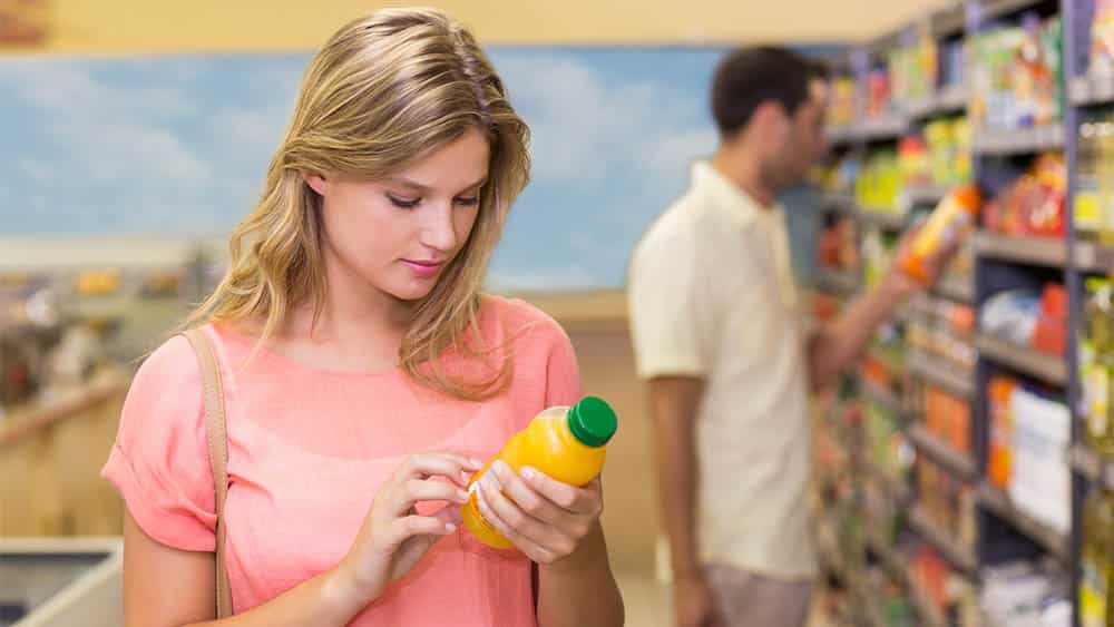 Mulher em supermercado lendo rótulo de um suco em garrafa.