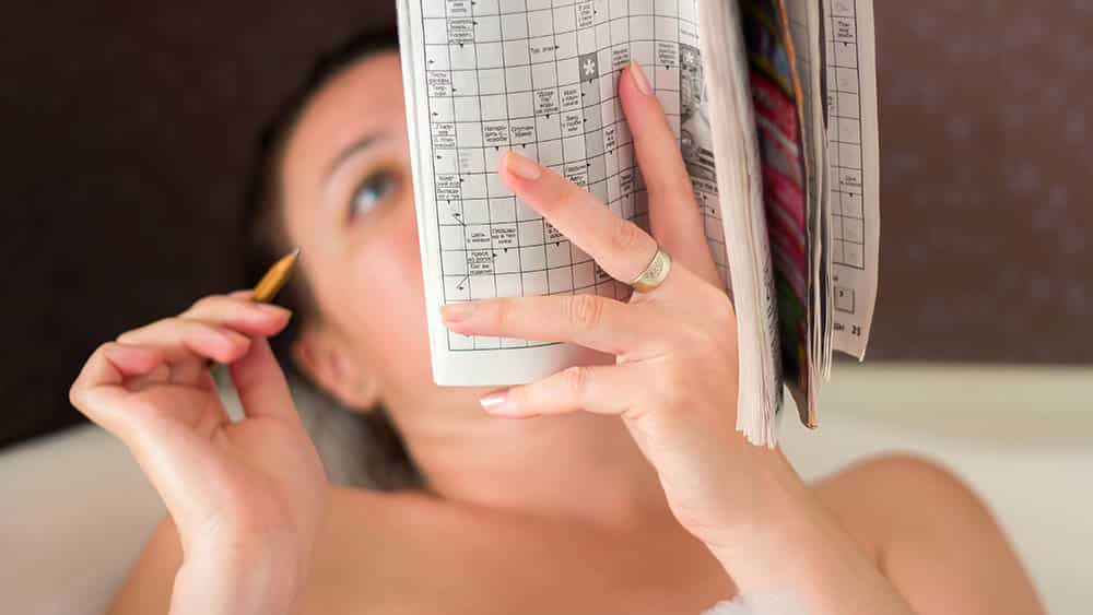 Mulher deitada fazendo palavras cruzadas, um dos melhores exercícios para o cérebro.