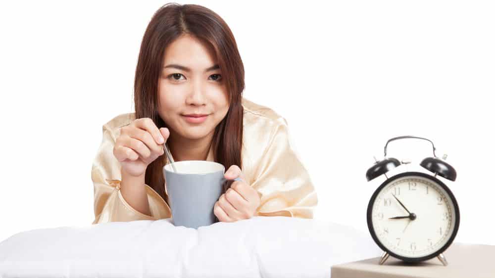 moça deitada diante de despertador com xícara de café. café interfere no sono