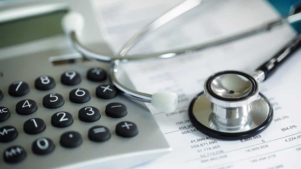 estetoscópio e calculadora sobre uma mesa indicando os altos custos da saúde