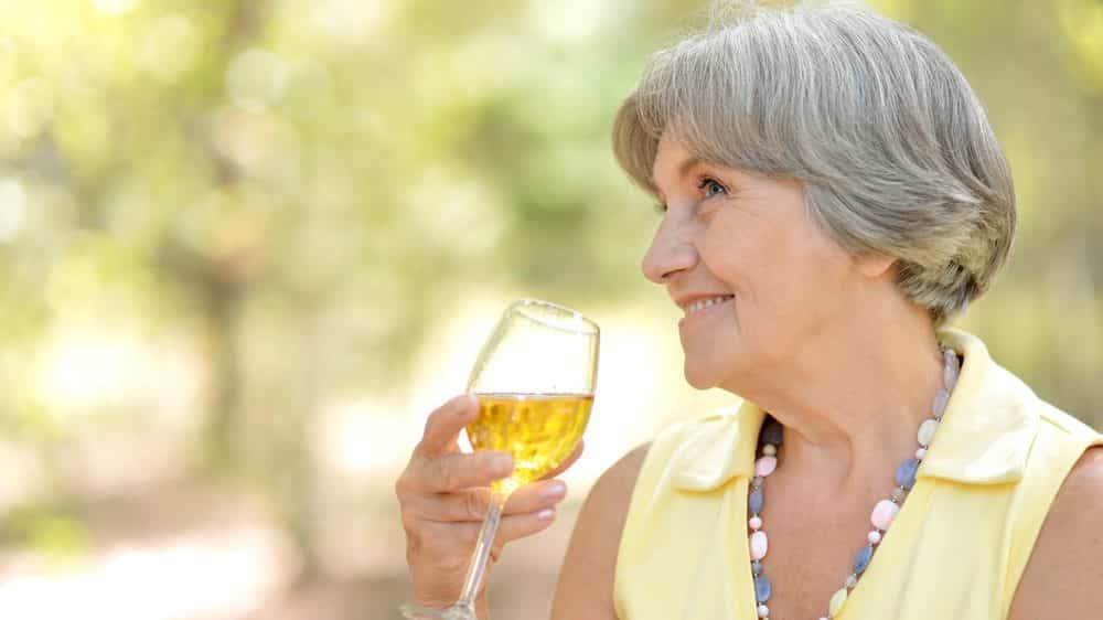 idosa feliz, com taça de vinho na mão. Veja a história de dona Ana.