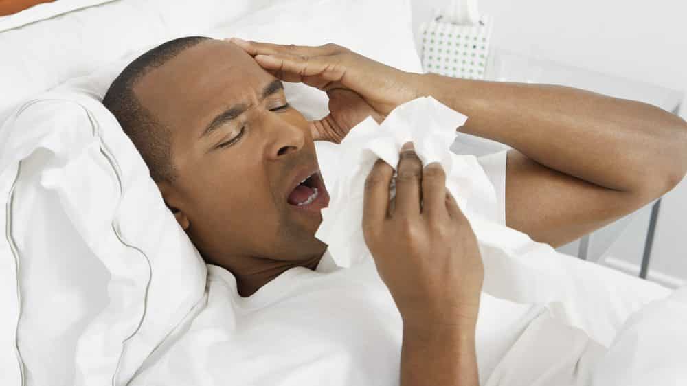 Homem com gripe deitado e espirrando.