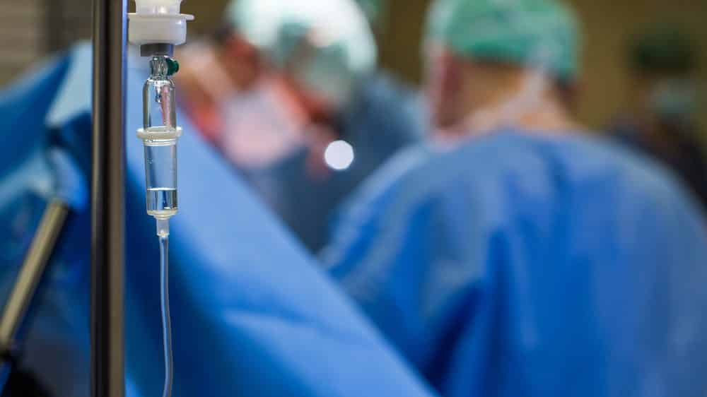 foco em gotejamento de soro, com cirurgia ao fundo. quais os limites do SUS?