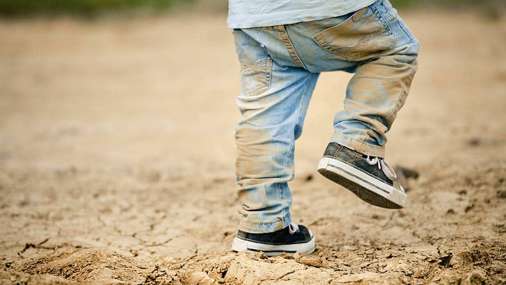Menino brincando em chão de terra com jeans sujo. Relação entre germes e asma vem sendo estudada.