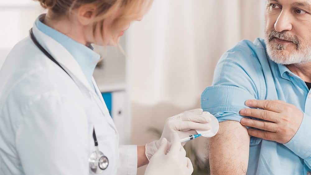 Febre amarela | Artigo Médico aplicando uma vacina contra febre amarela no braço de um senhor de meia idade.