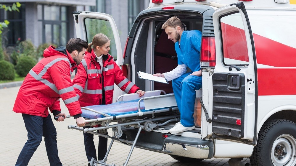Socorristas retiram maca da ambulância para atender paciente.