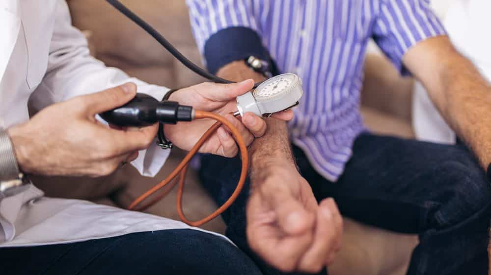 médico afere a pressão de paciente com hipertensão arterial