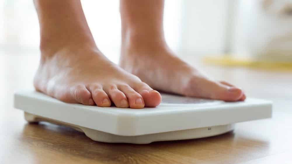 mulher se pesando em balança. o paradoxo da obesidade mostra