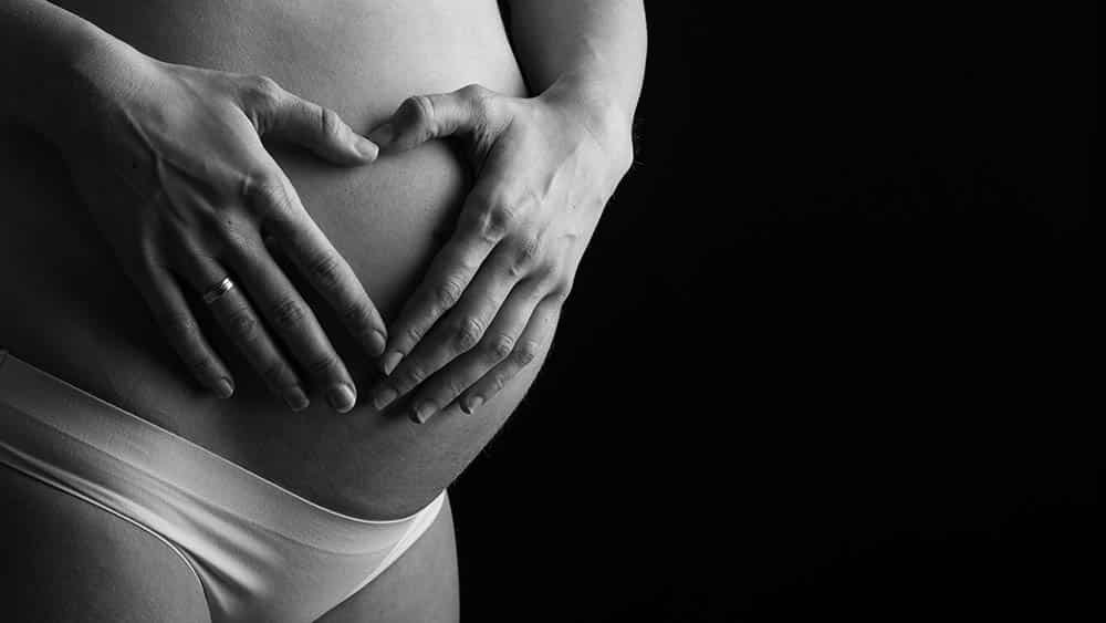 mulher grávida com a mão na barriga. veja relação entre gravidez e coronavírus