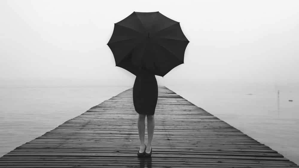 mulher em pé em uma ponte, segurando um guarda-chuva. Muitas vezes, a angústia não tem causa aparente