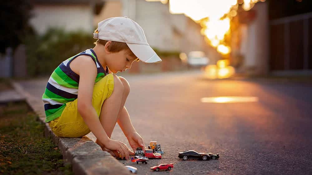 menino brinca com carrinhos no meio fio. Felicidade plena, só experimentamos na infância