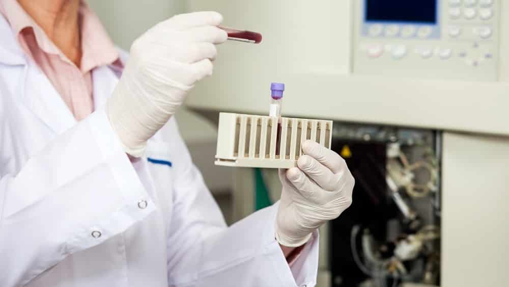 Mulher em laboratório com luvas cirúrgicas guardando um tubo de ensaio com sangue.
