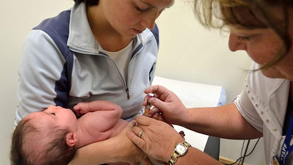 Mãe segurando bebê para tomar vacina contra sarampo. Houve aumento da mortalidade infantil e materna