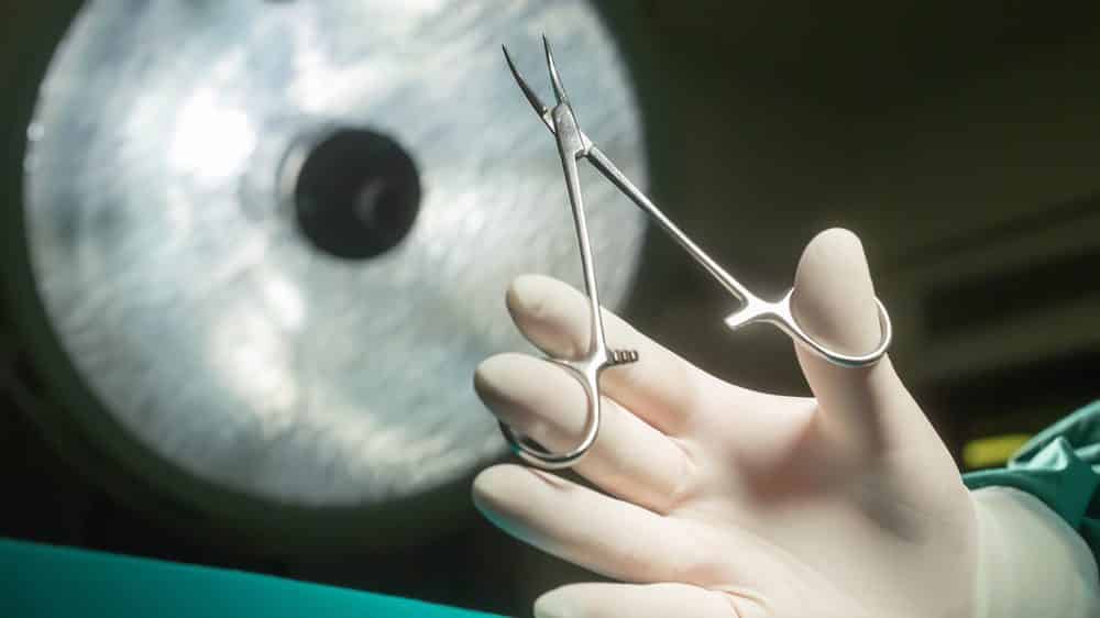 mão de médico segurando tesoura cirúrgica