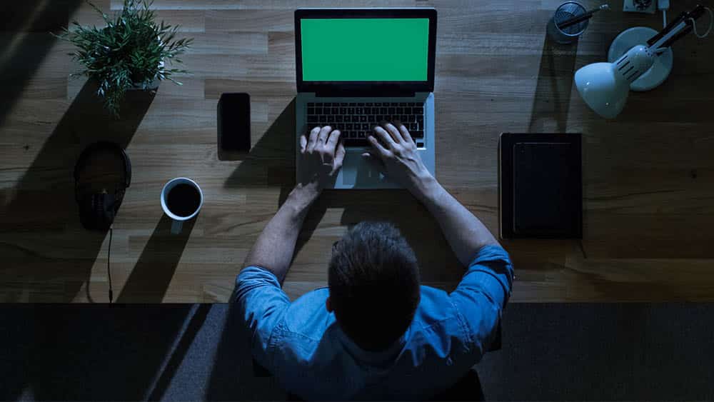Vista de cima de um homem trabalhando no computador no escuro. Avanços tecnológicos aumentam a carga de trabalho