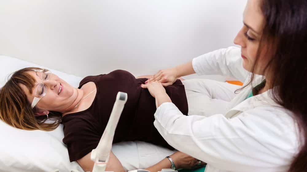 mulher na menopausa deitada em cama é examinada por médica ginecologista
