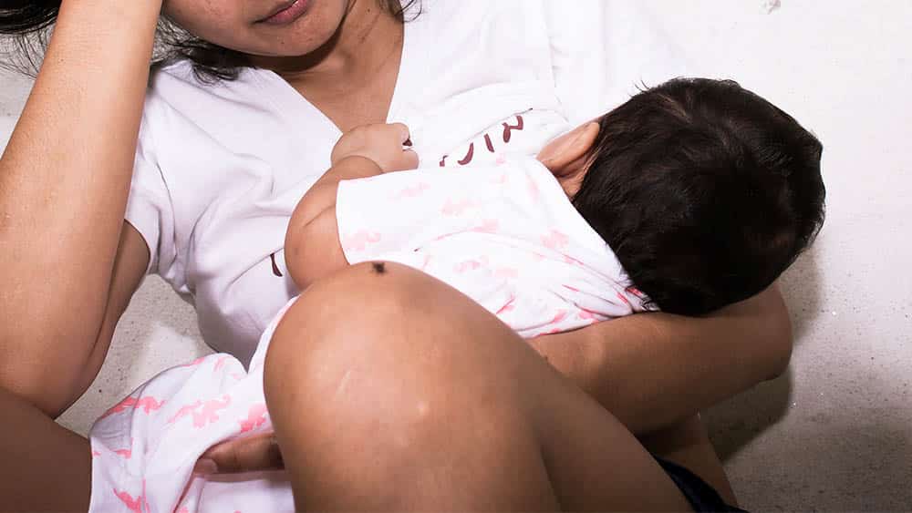 Menina adolescente com bebê mamando e uma mão na cabeça indicando preocupação.