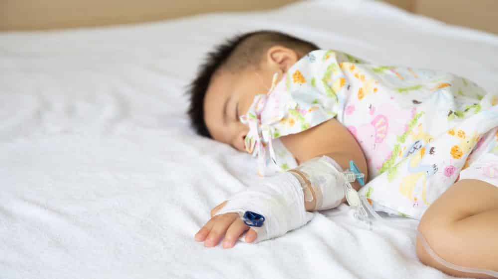 Criança com meningite dormindo em cama hospitalar enquanto toma soro.