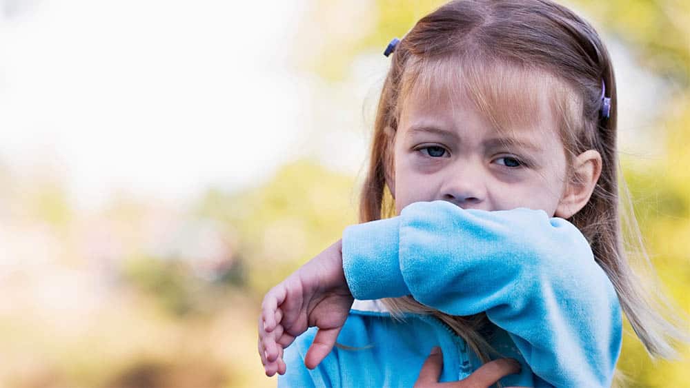 Menina com olhos de coriza limpando a boca com o braço.