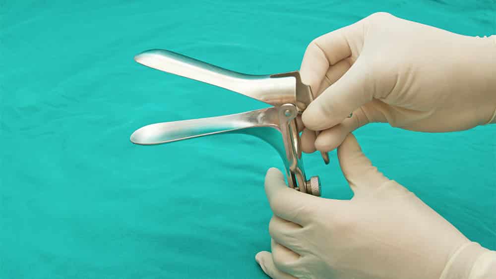 Mãos com luvas segurando um espéculo vaginal.