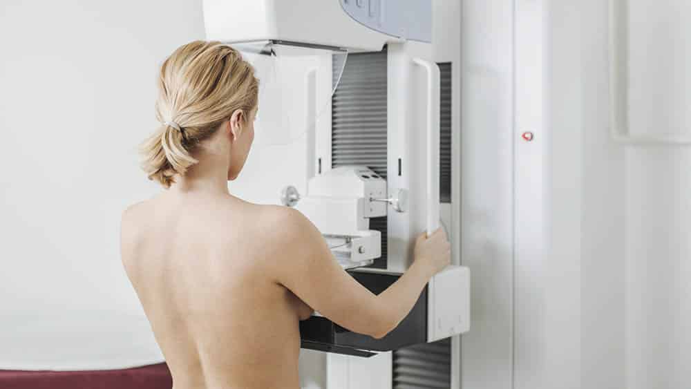 Mulher de costas fazendo mamografia.