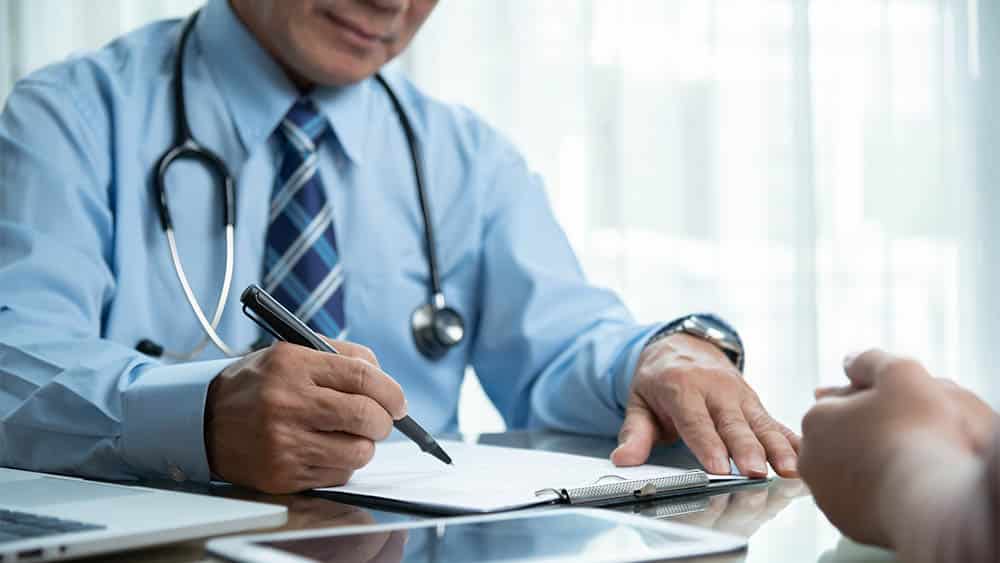 Médico em consulta com paciente escrevendo prescrição.