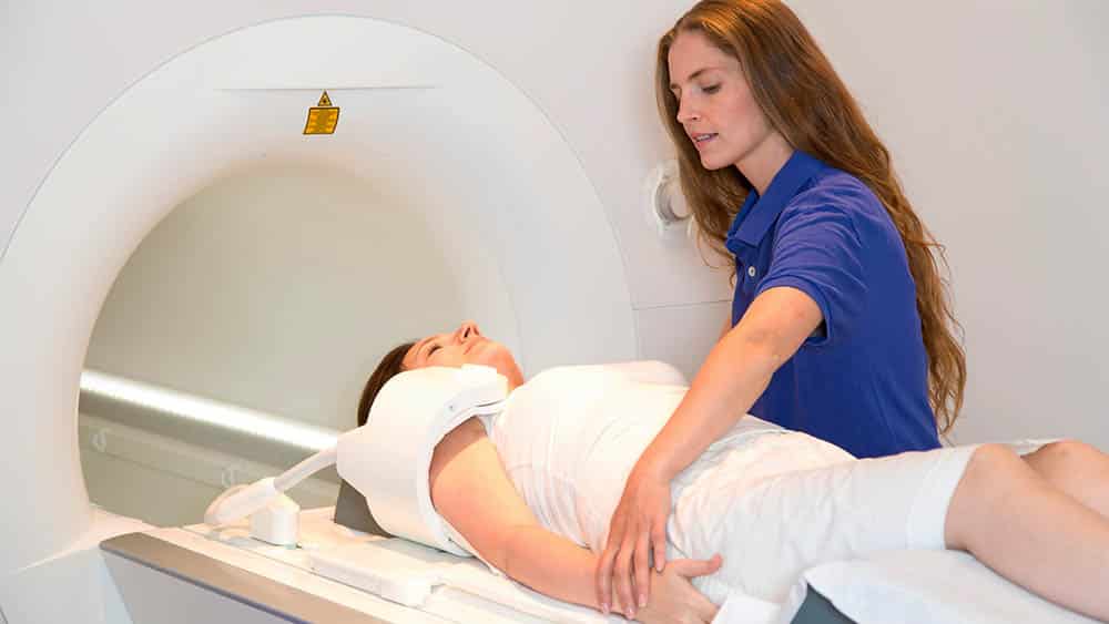 Assistente preparando mulher que vai fazer ressonância magnética do ombro.