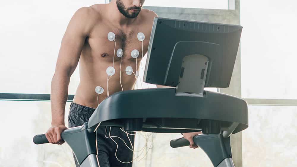Homem com eletrodos no tórax fazendo teste ergométrico em esteira.