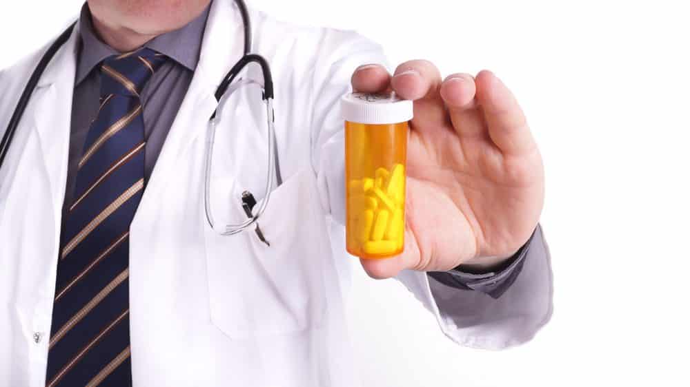 Médico segurando frasco de medicamento. Propaganda enganosa de remédios coloca em risco a saúde da população.