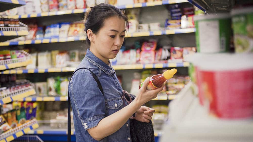 Mulher em supermercado segurando produto e olhando rótulos de alimentos.