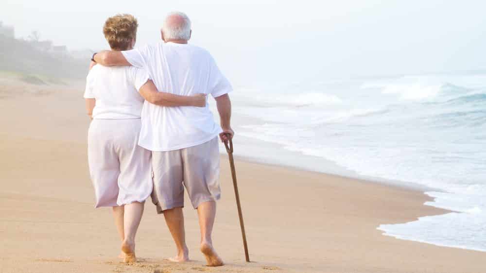 Prevenir ou remediar - envelhecimento e saúde | Artigo casal de idosos andando na praia. Envelhecimento e saúde podem andar juntos
