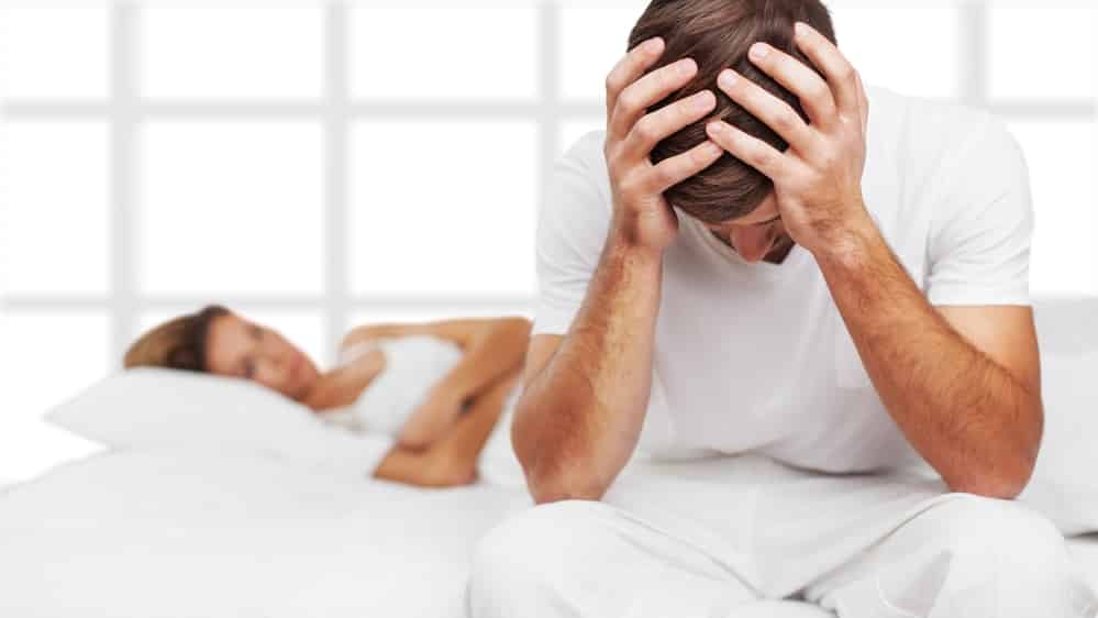 homem sentado na beira da cama, com cabeça escondida nas mãos, ao lado de mulher deitada; conheça a história de Paulão, o patriota