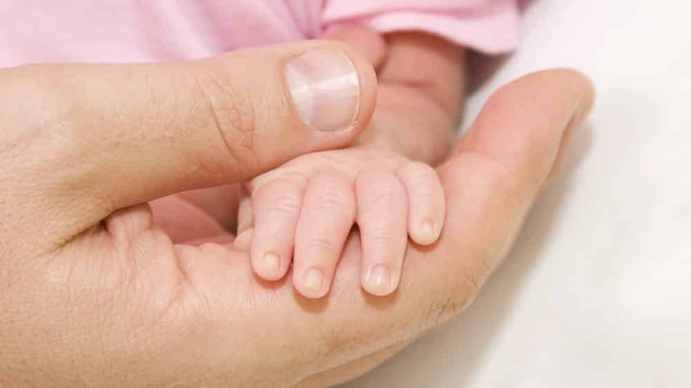 mão de homem segurando mão de bebê. Incidência da sífilis congênita é alta no Brasil.