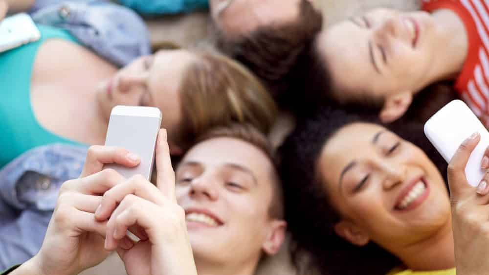 Entre adolescentes sedentários, meninas são mais inativas | Coluna jovens deitados em círculo, olhando o celular. sedentarismo na adolescência é prejudicial à saúde