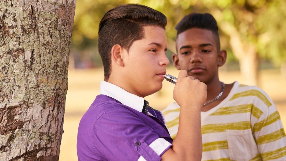 adolescente fuma cigarro eletrônico ao lado de amigo. Uso de cigarro eletrônico na adolescência traz sérios riscos à saúde