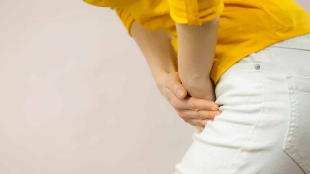 Mulher com blusa amarela sofre de dor causada por infecção urinária.