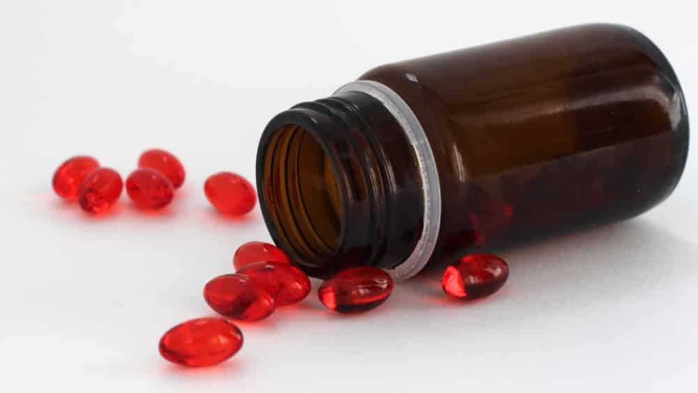 Pote de ibuprofeno caído com cápsulas vermelhas de gel espalhadas ao redor.