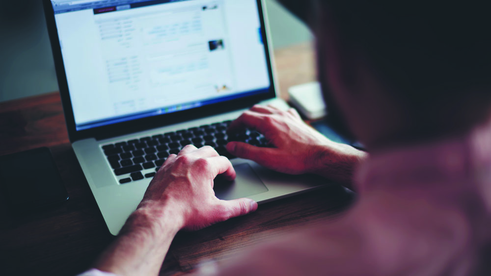 Homem trabalhando em casa com notebook. Organizar a estação de trabalho é uma das dicas para lidar com o home office na quarentena.