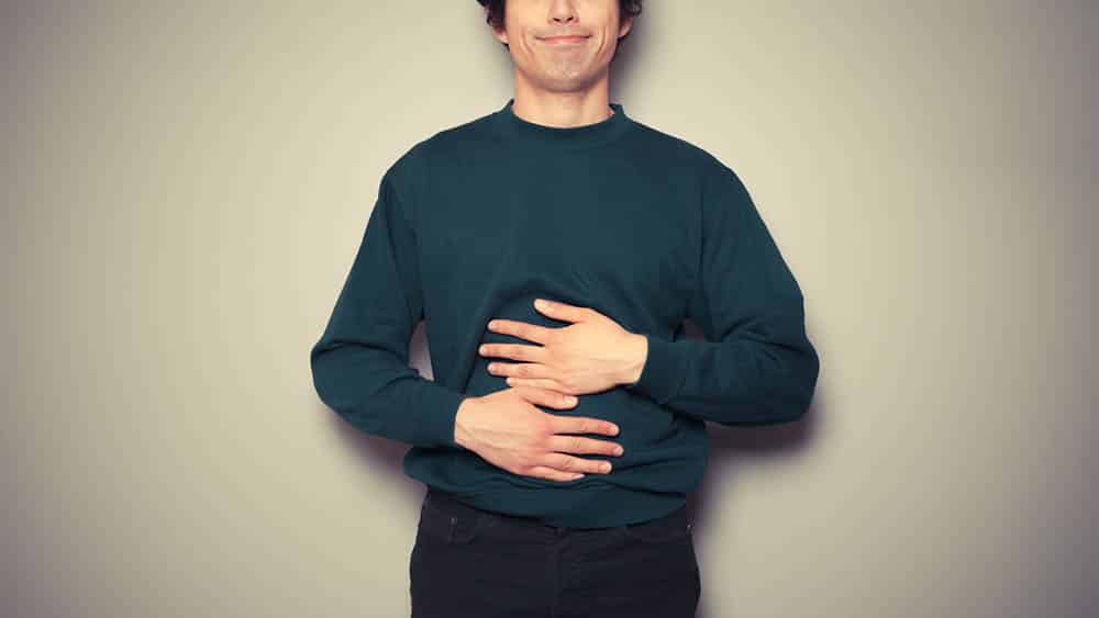 Homem esfregando a barriga indicando saciedade após comer.