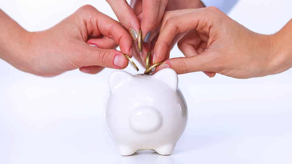 Várias mãos colocando moedas em um cofre porquinho.