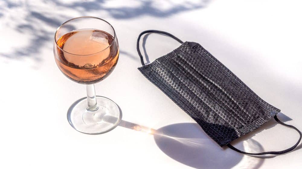 copo de vinho e máscara preta sobre a mesa ao ar livre. Uso de álcool na quarentena pode ser abusivo
