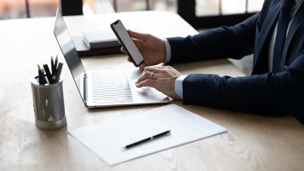 close de homem sentado à mesa de escritório diante do computador e do celular. Vida virtual ficou mais intensa com a pandemia