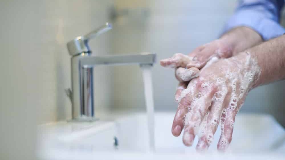 close em mãos de homem ensaboadas lavando a mão na pia. Essa é uma das recomendações sobre a covid-19