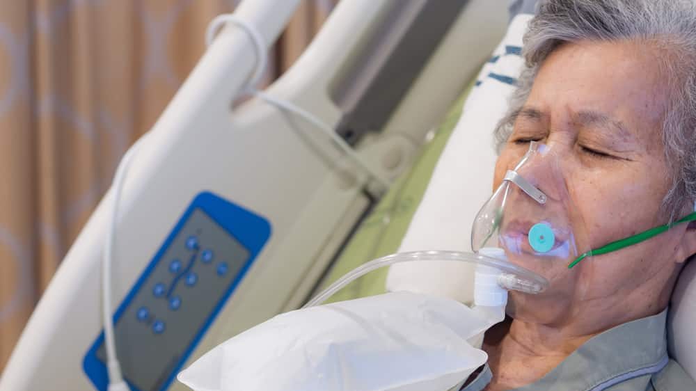 mulher idosa em leito hospitalar, com máscara de oxigênio para tratar edema pulmonar