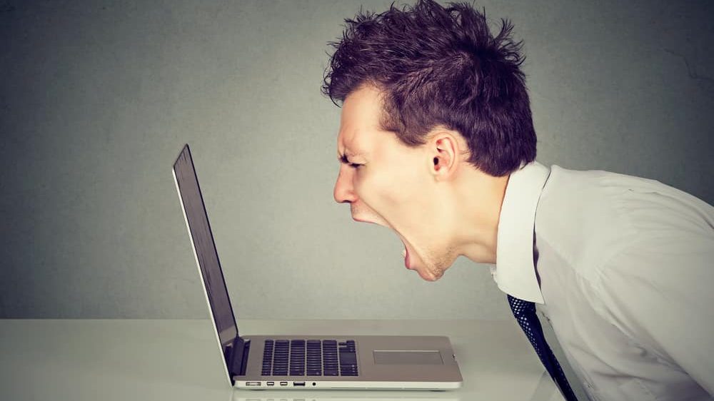 homem com ódio grita em frente à tela do computador