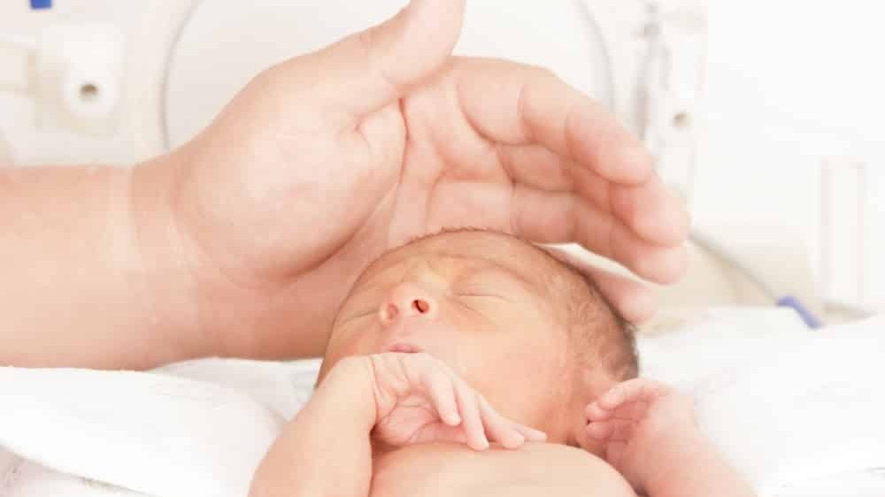 bebê prematuro na incubadora, com síndrome alcoólica fetal, e mão de adulto acariciando sua cabeça