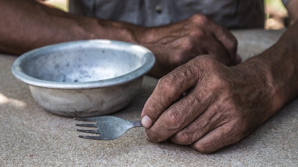 close em mãos de homem segurando garfo, apoiadas em mesa com prato vazio. epidemia causou a fome de milhares de brasileiros