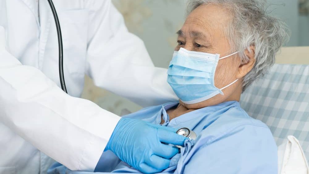 paciente com máscara em cama de hospital, sendo auscultado por médico. entenda a evolução da covid-19